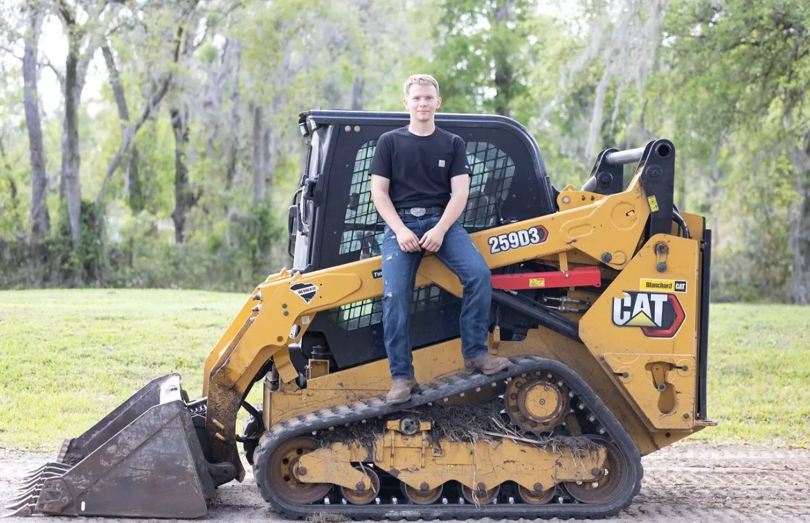 Owner of Imagine Land Works standing on a CAT skid steer track loader