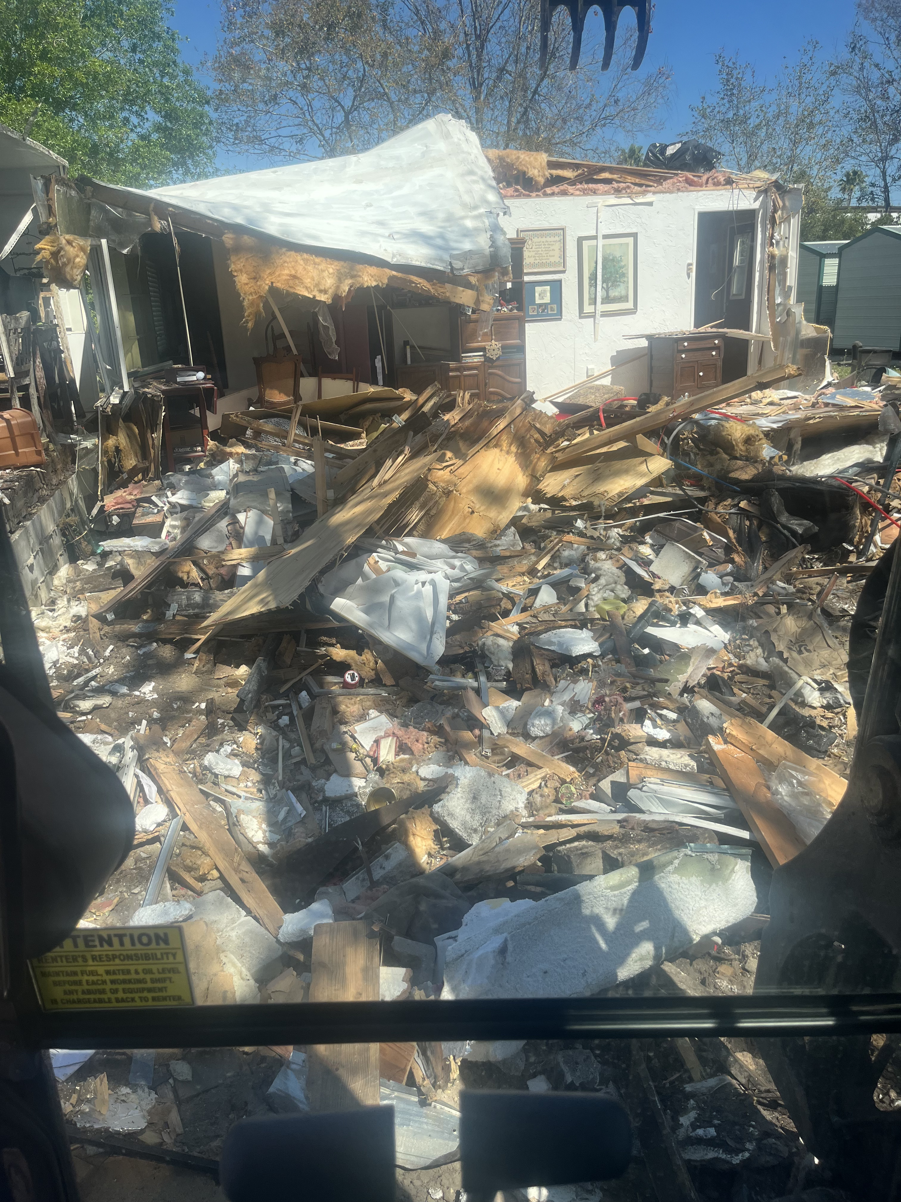 Collapsed roof and interior debris pile mid-teardown during a mobile home demolition