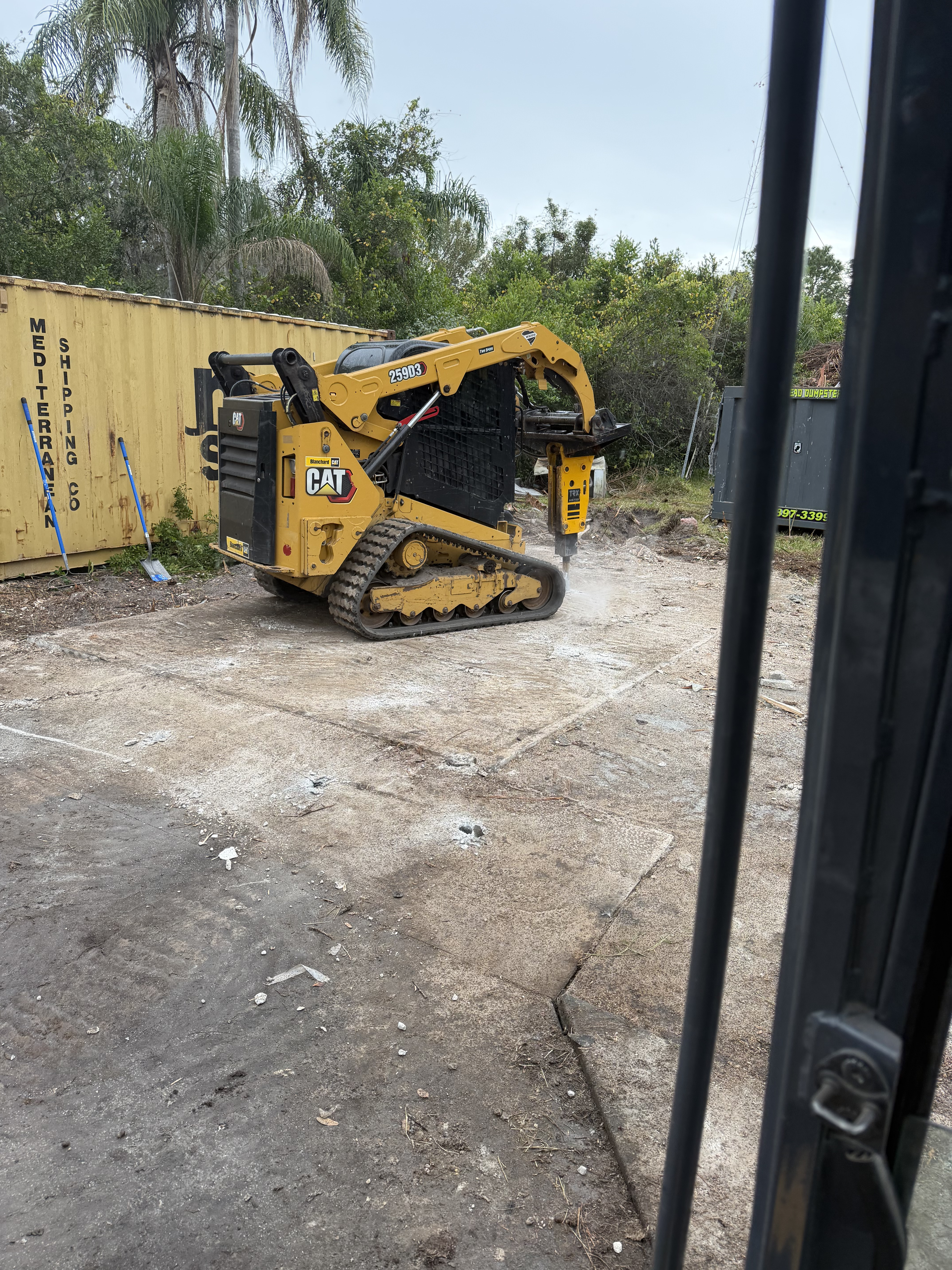 CAT skid steer with hydraulic breaker attachment demolishing a concrete slab