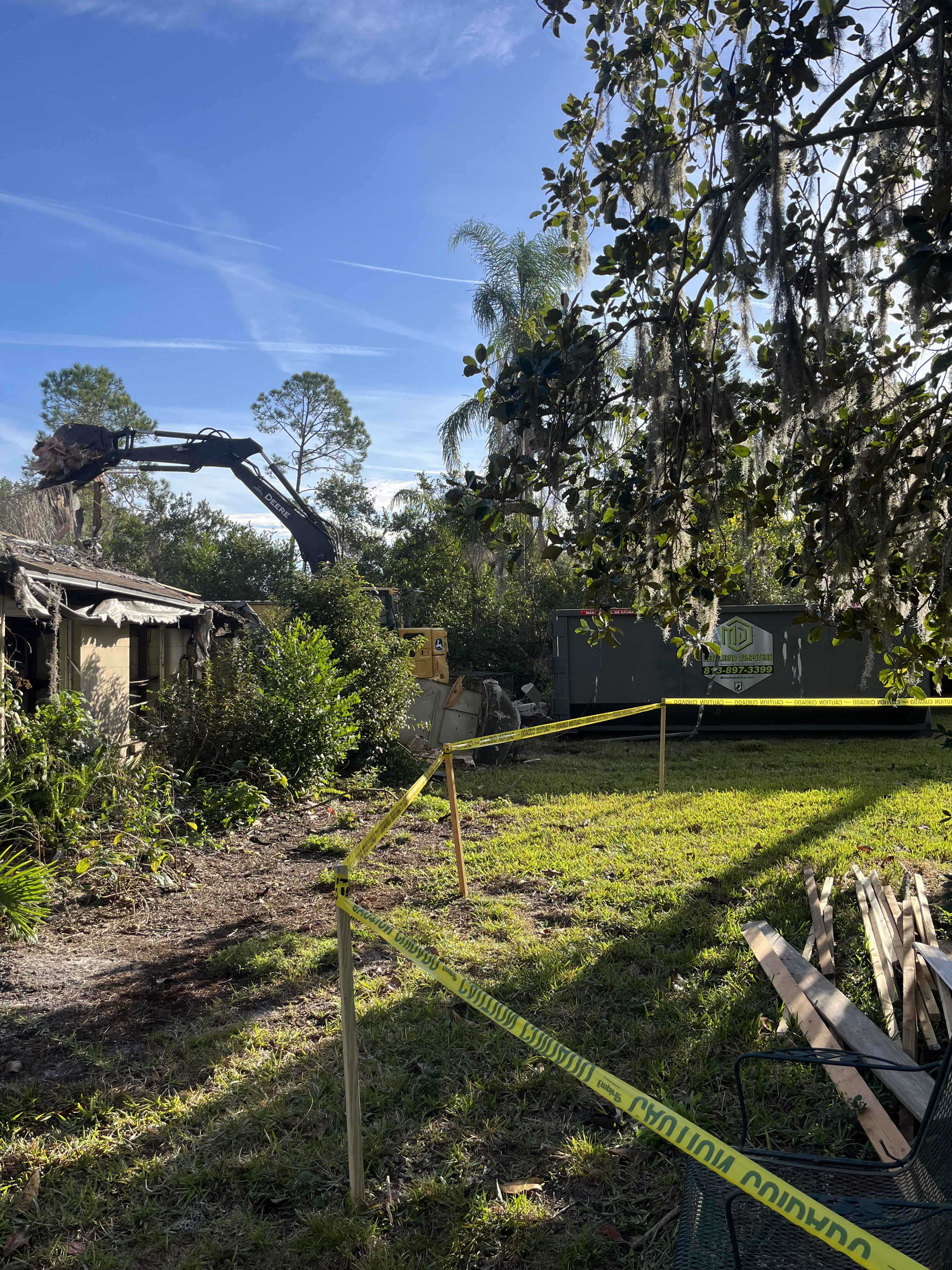 Demolition site secured with caution tape as an excavator clears structure debris
