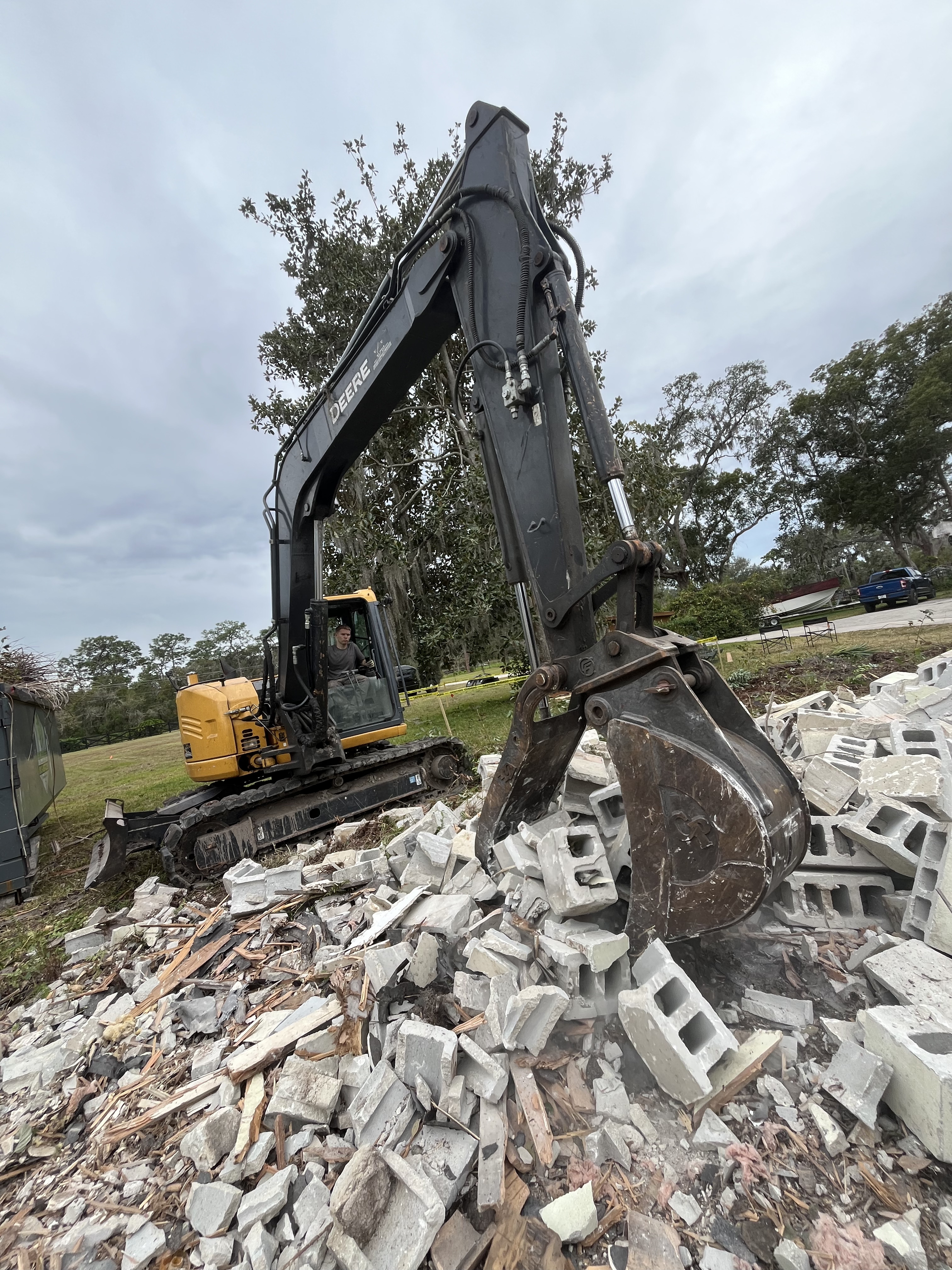 Excavator bucket clearing a pile of broken cinder block from a demolished wall
