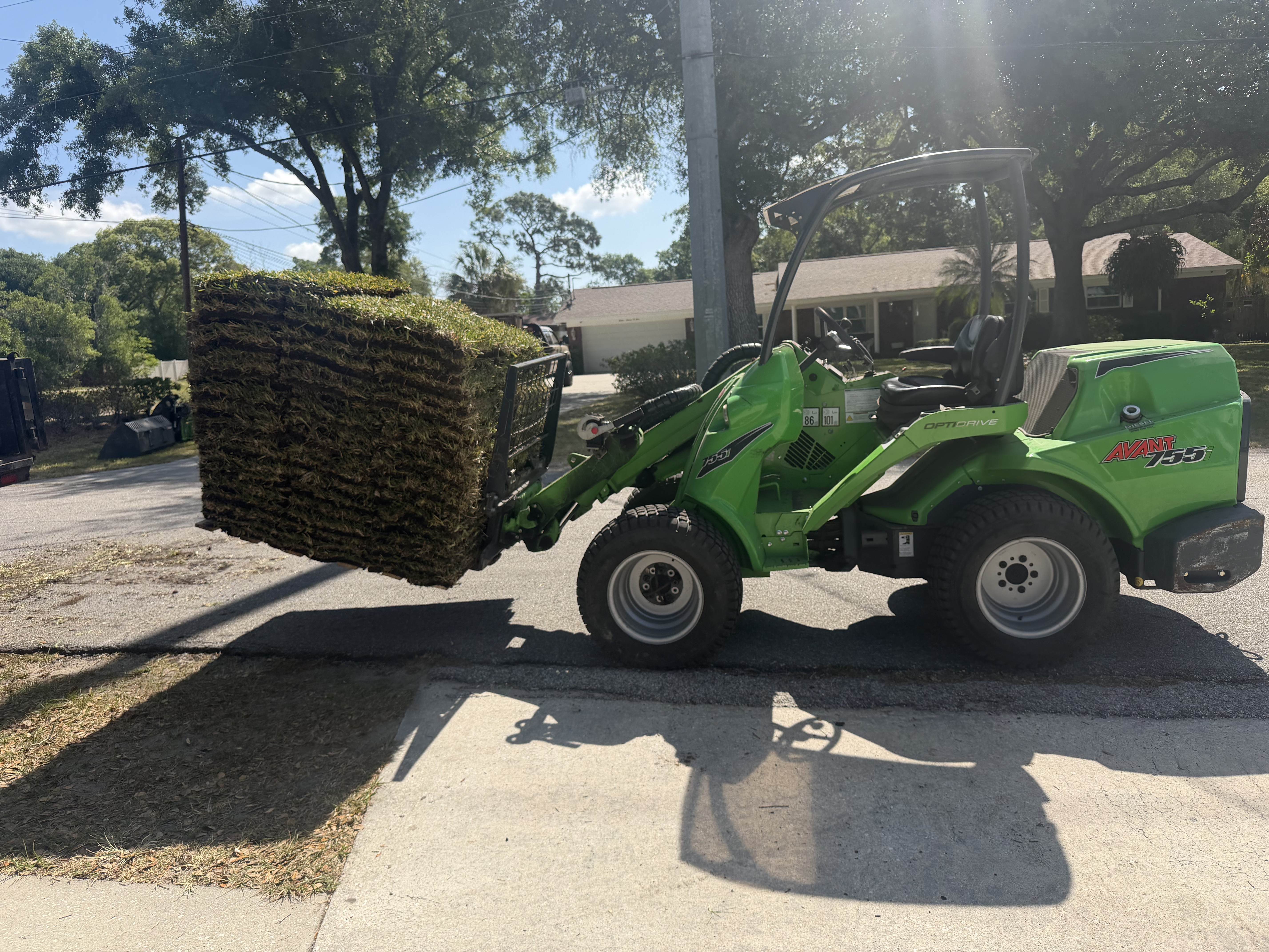 Compact loader delivering a pallet of sod rolls for installation